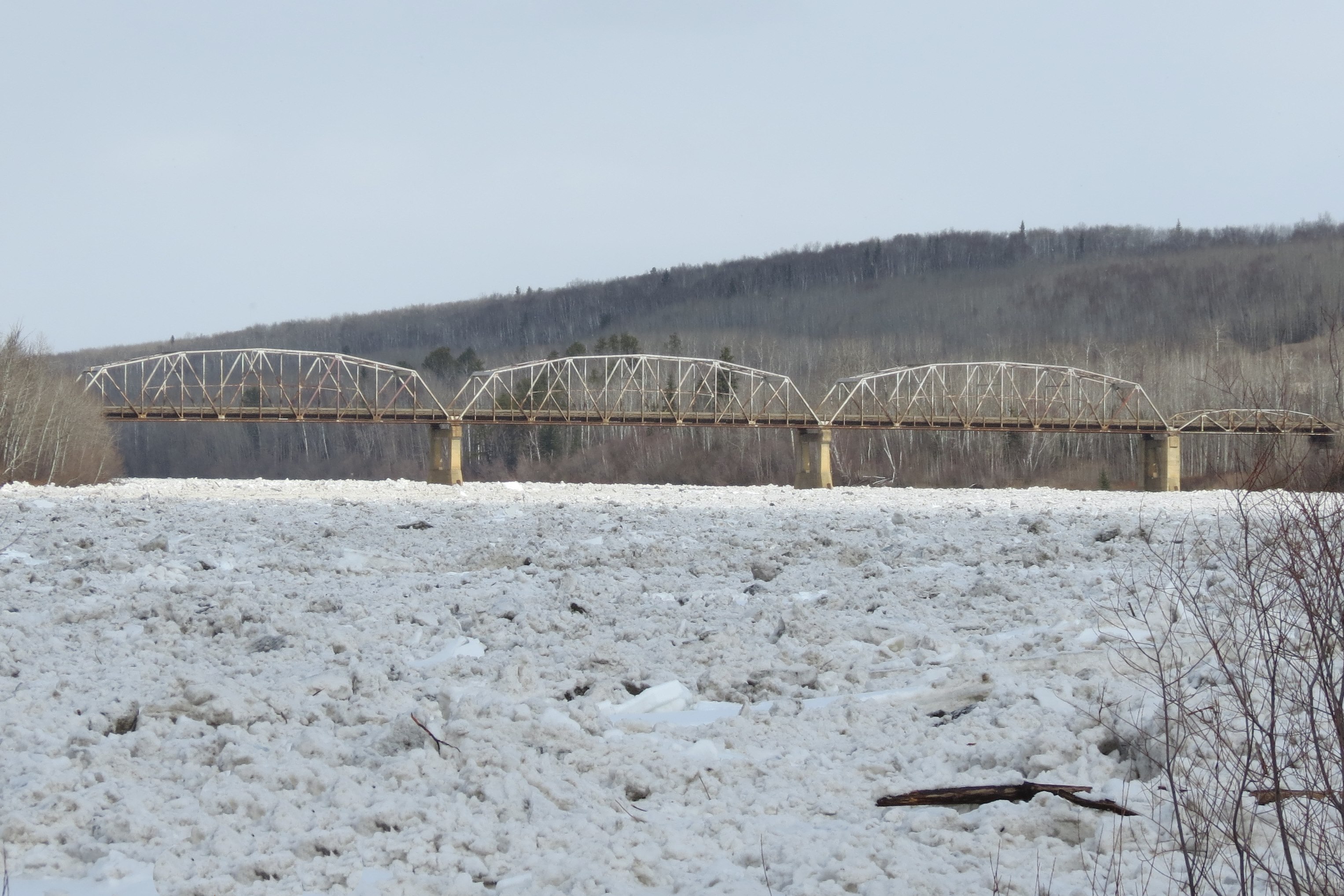 Photograph of an ice jam in a river with a truss-style bridge in the background.