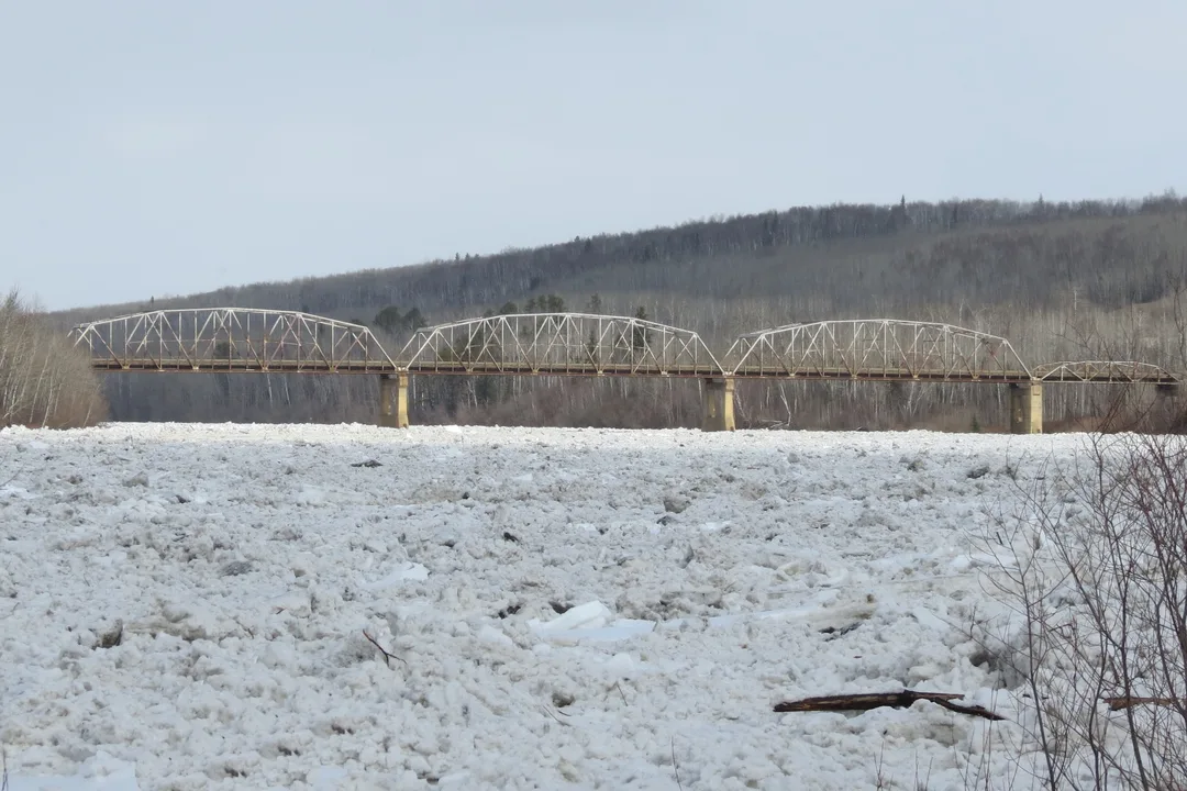 Photograph of an ice jam in a river with a truss-style bridge in the background.