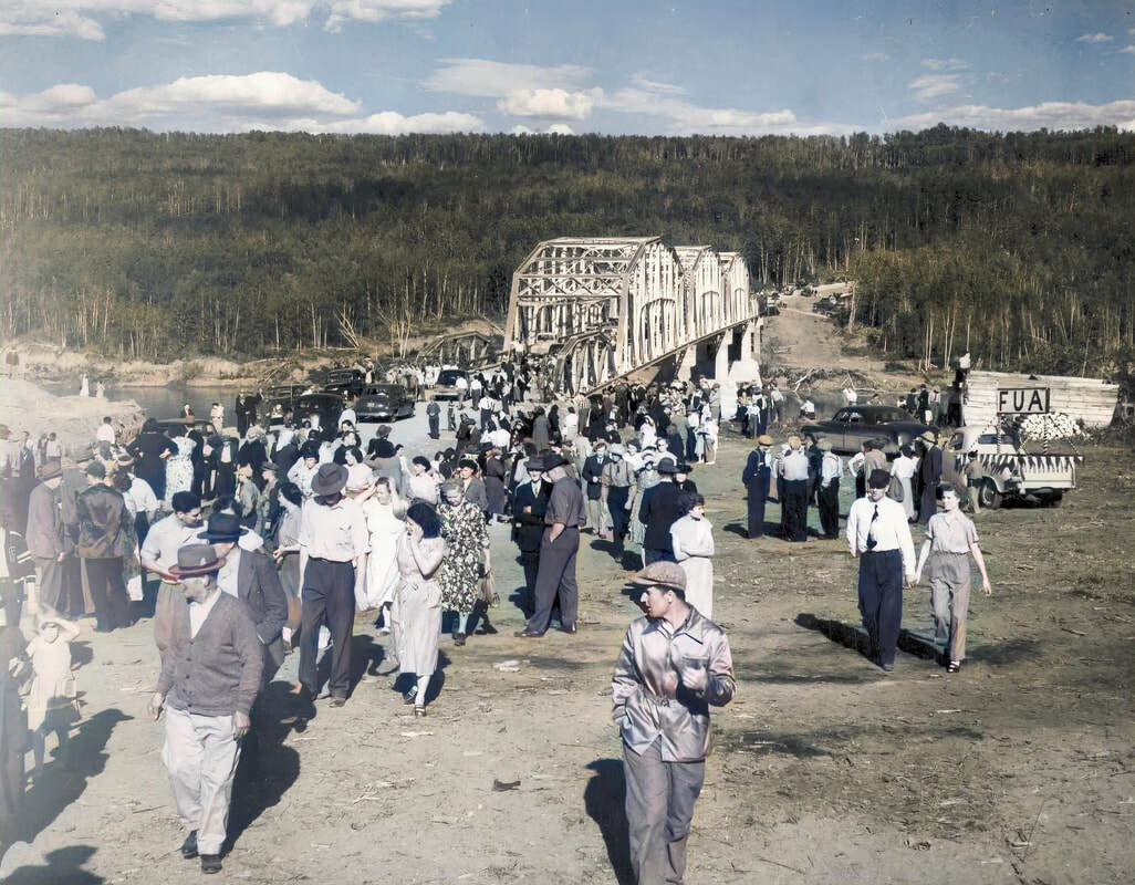 Colourized photograph taken in 1952 of a large group of people walking away from a bridge. A parade float on the back of a pickup truck is in the background and there are cars parked on the approach to the bridge.