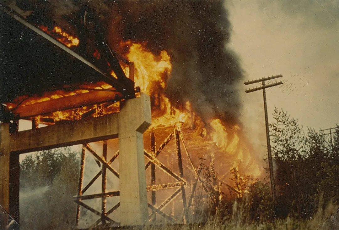 Taken from below a bridge, photograph of a fire raging in the structure and deck of the bridge.